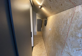 Pasillo inclinado en un lodge con paredes y techo de madera, iluminación moderna y una puerta al fondo.