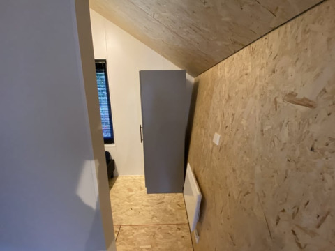 Et billede af et lille værelse i en lodge med skrå loftvæg, træpaneler og et skab mod væggen.