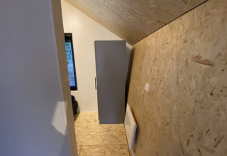 Et billede af et lille værelse i en lodge med skrå loftvæg, træpaneler og et skab mod væggen.