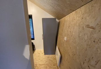 Photo d’une petite chambre de lodge avec plafond en bois incliné et armoire placée contre le mur latéral.
