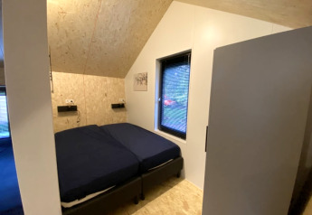 Lodge bedroom with angled wooden ceiling, twin beds with dark linen, window, and minimalist decor.