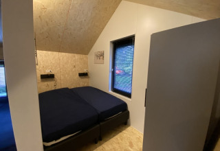 Dormitorio de cabaña con techo inclinado de madera, dos camas, ventana y una decoración minimalista.