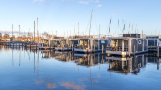 Modernas casas flotantes en Marina Parcs Naarden, Países Bajos, reflejadas en el agua bajo el cielo azul.