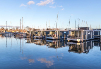 Modern houseboats at Marina Parcs Naarden in the Netherlands reflecting on calm water under a blue sky.
