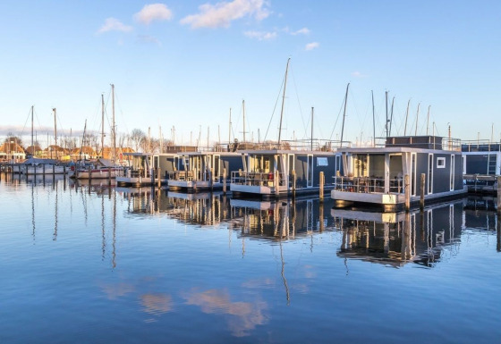 Modernas casas flotantes en Marina Parcs Naarden, Países Bajos, reflejadas en el agua bajo el cielo azul.