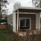 Et moderne tiny house med overdækket terrasse og badetønde i haven, omgivet af grønne planter og buske.