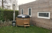 Klein houten huisje met twee ramen en een ronde buiten hottub op het gras naast het huis.