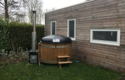 Tiny wooden house with two windows and a round outdoor hot tub on the lawn next to the house.