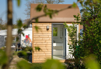 Foto all'aperto di una moderna cabina glamping in legno con porta aperta e biciclette sullo sfondo.
