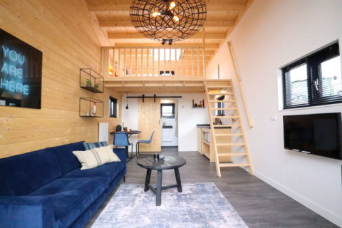 Alojamiento glamping moderno con altillo, interior de madera, sofá azul, comedor y cocina.