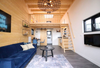 Alojamiento glamping moderno con altillo, interior de madera, sofá azul, comedor y cocina.