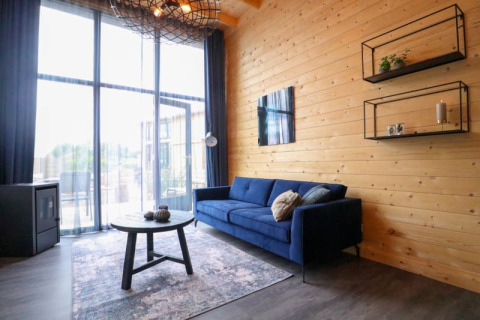 Hébergement glamping moderne avec canapé bleu, mur en bois, grandes fenêtres et décoration chaleureuse.