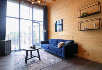 Hébergement glamping moderne avec canapé bleu, mur en bois, grandes fenêtres et décoration chaleureuse.