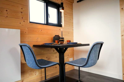 Coin repas moderne avec deux chaises bleues et une petite table dans un hébergement glamping en bois.