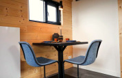 Moderne eethoek met twee blauwe stoelen en kleine tafel in een glamping-accommodatie met houten wanden.