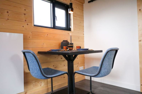 Moderne eetruimte met twee blauwe stoelen bij een kleine tafel in een glampingverblijf met houten muren.