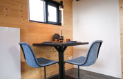 Moderne eethoek met twee blauwe stoelen en kleine tafel in een glamping-accommodatie met houten wanden.