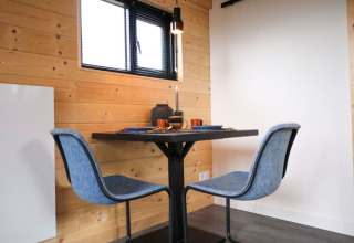 Moderne eetruimte met twee blauwe stoelen bij een kleine tafel in een glampingverblijf met houten muren.