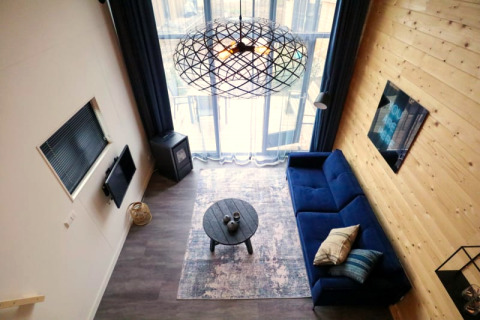 Hébergement glamping moderne avec canapé bleu, table ronde et grandes fenêtres, vue du dessus.