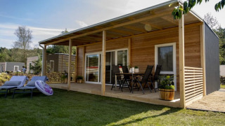 Casa in legno moderna con veranda coperta, mobili da giardino e prato verde circostante.