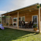 Et moderne træhus med terrasse og havemøbler, omgivet af grønne græsplæner og natur i baggrunden.