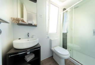 Baño moderno en un lodge con lavabo, inodoro, espejo y amplia ducha cerrada de cristal, luminoso y limpio.