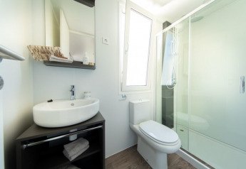 Moderne lodge-badeværelse med vask, toilet, spejl og en stor bruser bag glasdør, lyst og rent.