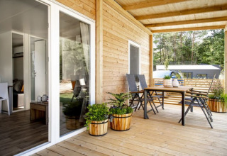 Houten veranda van een moderne lodge met tafel, stoelen en planten, omgeven door bos en rust.