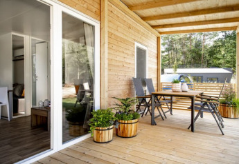 Veranda in legno con tavolo, sedie e piante in vaso presso un lodge moderno immerso nella natura verde.