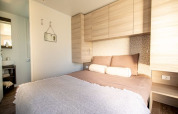 Moderne lodge-soveværelse med dobbeltseng, lyse træmøbler, vægskab og synligt badeværelse i baggrunden.