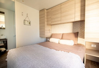 Chambre de lodge moderne avec grand lit, armoires en bois clair et aperçu d’une salle de bain attenante.
