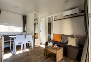 Modern lodge-interieur met eetruimte, zetel, salontafel en toegang tot een slaapkamer, helder ingericht.