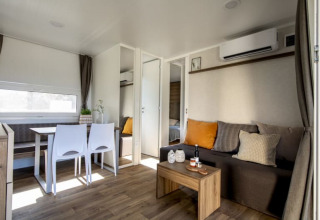 Moderne lodge-interieur met eethoek, bank, salontafel en toegang tot een slaapkamer, licht ingericht.