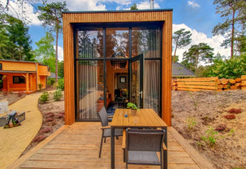Piccola casa in legno con grandi vetrate e terrazza esterna, immersa nella natura e circondata da alberi.