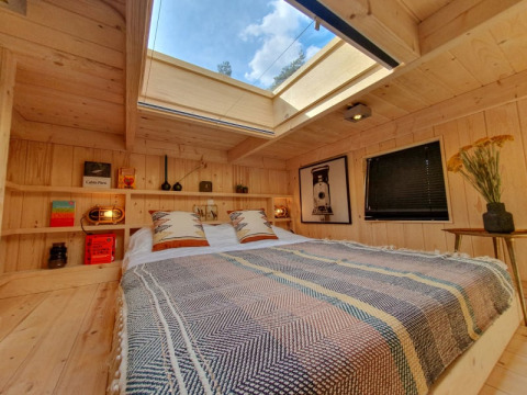 Cozy tiny house bedroom with skylight, wooden walls, books on shelves, and comfortable bedding.
