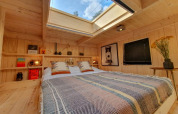 Cozy tiny house bedroom with skylight, wooden walls, books on shelves, and comfortable bedding.