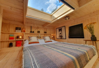 Acogedor dormitorio en una tiny house con tragaluz, paredes de madera, libros y detalles decorativos.