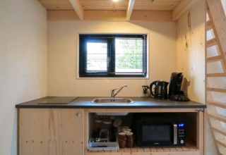 Tiny house kitchenette with sink, electric kettle, coffee maker, microwave, and wooden shelves.