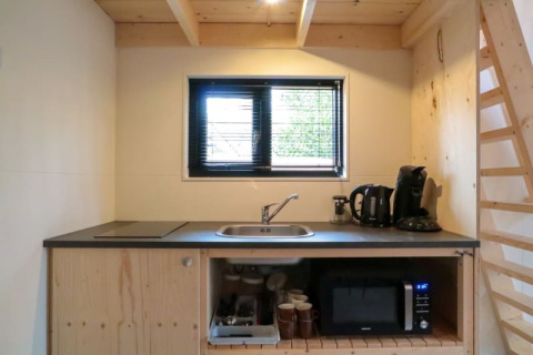 Pequeña cocina en una tiny house con fregadero, hervidor, cafetera, microondas y estantes de madera.
