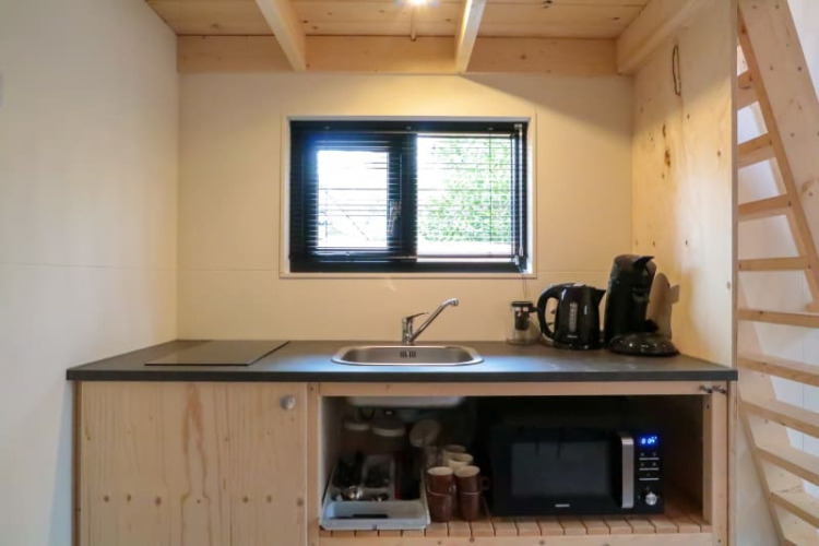 Petite kitchenette dans une tiny house avec évier, bouilloire, cafetière, micro-ondes et étagères en bois.