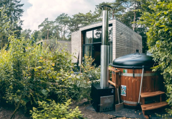 Photo d’un hébergement glamping moderne en forêt avec bain nordique entouré de verdure luxuriante.