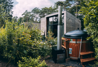 Foto van een modern glamping-verblijf in het bos met een hottub, omringd door weelderige planten.