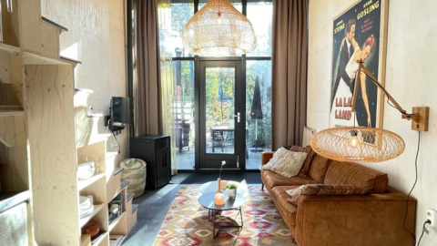 Small modern living room in a tiny house with brown sofa, colorful rug, pendant light, La La Land poster.