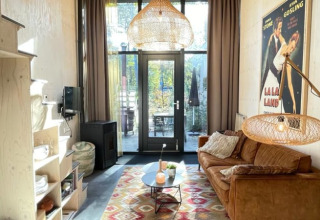 Petit salon moderne dans une tiny house avec canapé brun, tapis coloré, lampe suspendue et affiche La La Land.