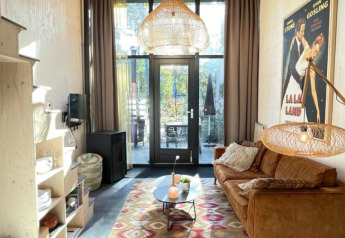 Petit salon moderne dans une tiny house avec canapé brun, tapis coloré, lampe suspendue et affiche La La Land.