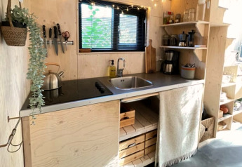 Piccola cucina in una tiny house con legno chiaro, scaffali aperti, lavello e piano cottura elettrico.
