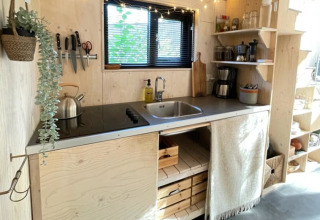 Cocina pequeña en una tiny house con madera clara, estanterías abiertas, fregadero y vitrocerámica.