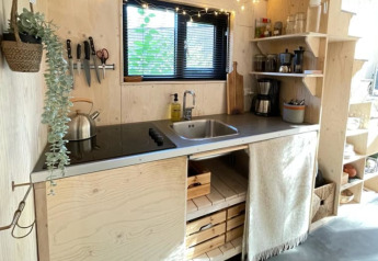 Kompakte Küche in einem Tiny House mit Holzdekor, Kochfeld, Spüle und offenen Regalen mit Geschirr.