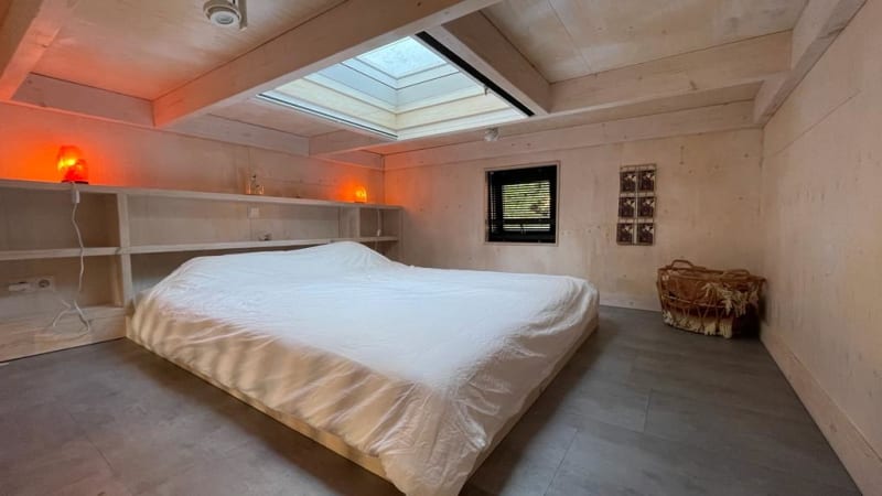 Chambre minimaliste dans tiny house avec puits de lumière, lit bas, étagères et lumières chaleureuses.