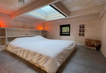 Camera minimalista in una tiny house con lucernario, letto basso, scaffali e luci accoglienti.